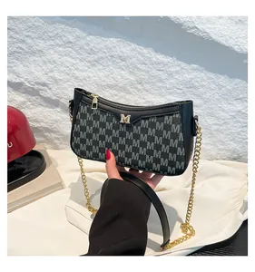Detail of crossbody bag with golden M hardware and black leather texture shown by hand