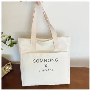Close-up of beige canvas tote bag featuring an outer pocket and minimalist black lettering
