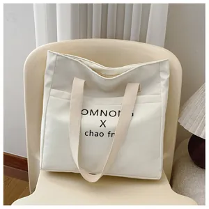 Detail view of white nylon tote bag with black letter print on a minimalist chair