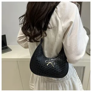 Detail of black faux leather hobo bag featuring crocodile texture and golden bow buckle