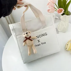 White canvas tote bag with letter print and brown knit bear charm on a desk