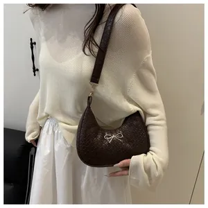Detail of dark brown woven shoulder bag with golden bow and half-moon structure on model