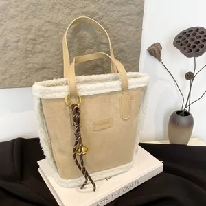 Beigefarbene Beuteltasche mit weißem Kunstpelzbesatz und goldener Glocke auf Buch