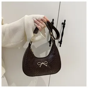 Macro detail of dark brown woven shoulder bag featuring a golden metal bow ornament