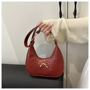 Close-up of a burgundy woven texture hobo bag featuring a gold metal bow detail