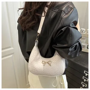 Close-up of white woven texture underarm bag with a golden bow metal buckle detail