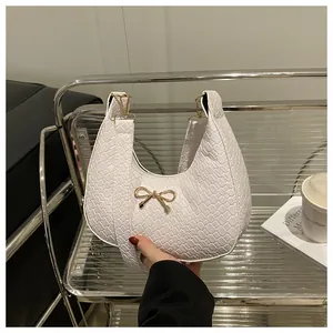 Close-up of white woven texture handbag with a golden bow metal clasp and shoulder strap