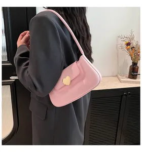 Dettaglio borsa sottobraccio rosa con chiusura a cuore dorata indossata su un blazer grigio