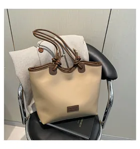Close-up of stylish large beige tote bag with brown straps on a black leather chair