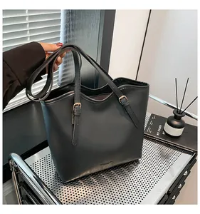 Detail of black matte leather tote bag featuring golden buckles and wavy top design