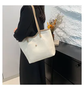 Vue latérale d'un grand sac fourre-tout crème avec bandoulière camel sur veste