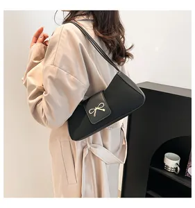 Detailansicht einer schwarzen Schultertasche aus Kunstleder mit goldener Schleifenschnalle