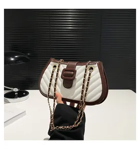 Detail of white quilted crossbody bag with brown leather trim and gold chain strap