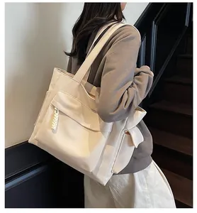 Detail of a beige canvas tote bag with front flap pocket and woven pompom pendant decor