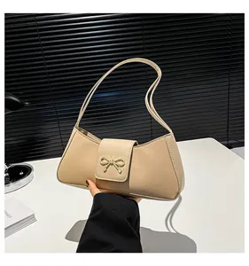Detailansicht einer beige Baguette-Tasche mit goldener Schleifenschnalle auf der Klappe