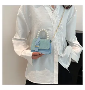Light blue glitter crossbody bag with pearl handle and gold chain strap on model