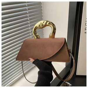 Dettaglio borsa in pelle marrone con manico dorato scultoreo e patta in pelle scamosciata