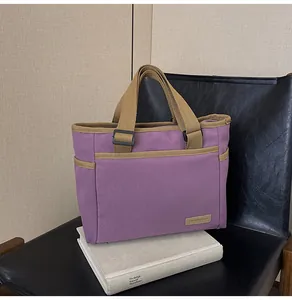Detail der lila Canvas-Tasche mit Seitentasche auf einem schwarzen Stuhl und Büchern