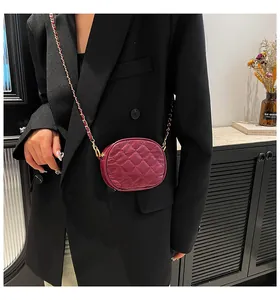 Detail of burgundy quilted mini chain bag worn over a black blazer for size scale