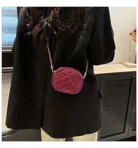 Detail of burgundy quilted crossbody bag with gold chain strap on a model shoulder