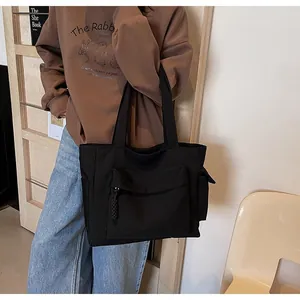 Detail view of a large black canvas tote bag with front pocket shown on a female model