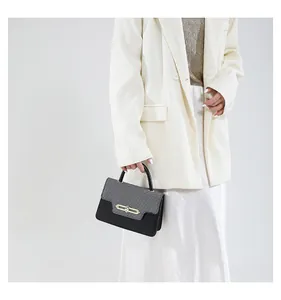 Detail showing the gray and black contrasting leather and gold lock of the square handbag