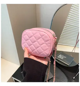 Macro detail of pink quilted mini crossbody bag with gold chain strap held by a hand
