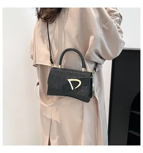 Detail of black crossbody bag featuring a glittery flap and matte gold D-buckle ornament