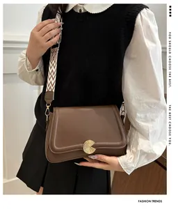 Detail of dark brown leather bag featuring golden circular buckle and wide woven strap