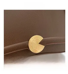 Close-up of litchi-grain brown leather handbag with gold circular metal buckle detail