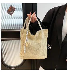 Close-up of beige woven straw tote bag featuring decorative ribbon and golden bell charm
