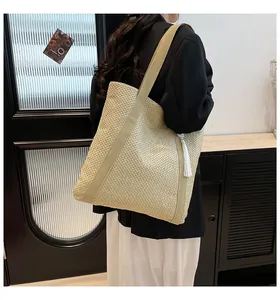 Détail d'un sac cabas en paille avec pompon blanc et bandoulière tissée sur mannequin