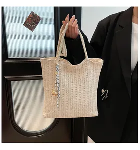 Detail of beige woven tote bag with vertical knit texture and a striped silk scarf charm
