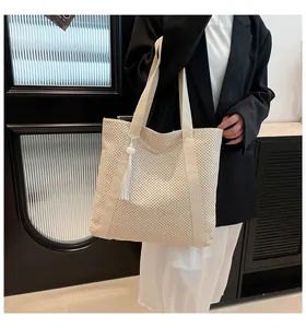 Gros plan du sac cabas en paille tissée avec anses crème et pendentif à pompon blanc