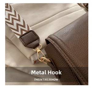 Detail of high-gloss gold metal hook and woven strap on brown lychee leather bag