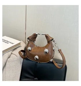 Detail of a brown leather crescent handbag featuring silver metal sphere decorations and handle