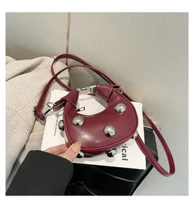 Detailed view of burgundy half-moon handbag with silver spherical rivets on white books