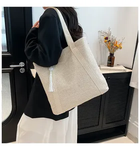 Détail d'un sac cabas en paille beige avec pompon et texture tressée sur un mannequin