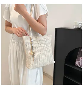 Detail of a creamy woven straw tote bag with vertical textures and a knotted pendant charm