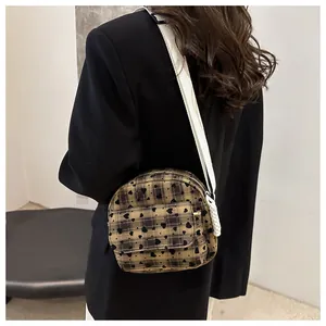 Detail view of a brown plaid saddle bag featuring black hearts and a white woven strap