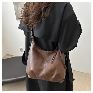 Detail der dunkelbraunen Hobo-Tasche mit matter Retro-Ledertextur getragen am schwarzen Mantel