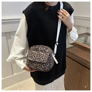 Detail of leopard print crossbody bag with white adjustable strap and woven zipper pull
