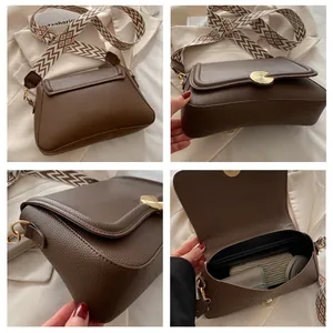 Detailed view of brown litchi pattern handbag with wide geometric strap and gold buckle