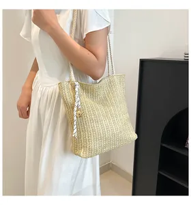 Straw shoulder bag detail featuring woven texture with white rope handles and bell charm