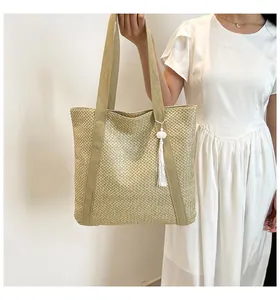 Détail d'un sac cabas en paille tissée avec texture diagonale et décor de pompon blanc