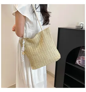 Detail of hand-woven straw tote bag with rope strap and decorative metallic pendant