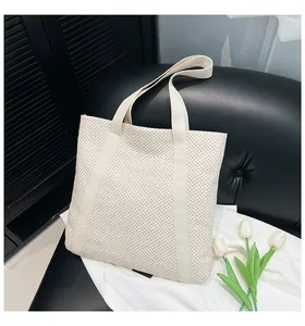Gros plan d'un sac cabas tissé beige avec texture 3D et larges anses sur un meuble
