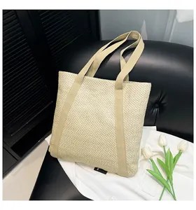 Gros plan d'un sac cabas en paille tressée beige avec anses renforcées sur un canapé noir