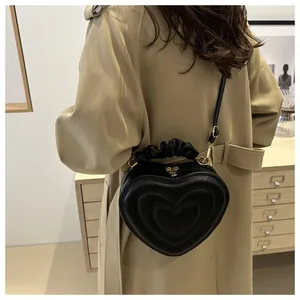 Chic black heart-shaped handbag worn with a trench coat showing style and gold hardware