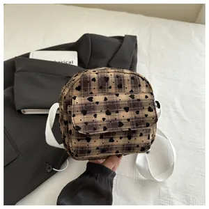 Detail of checkered crossbody saddle bag with heart patterns and wide woven shoulder strap